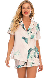 Blush pink botanical print satin pajama set with button-up top and shorts.