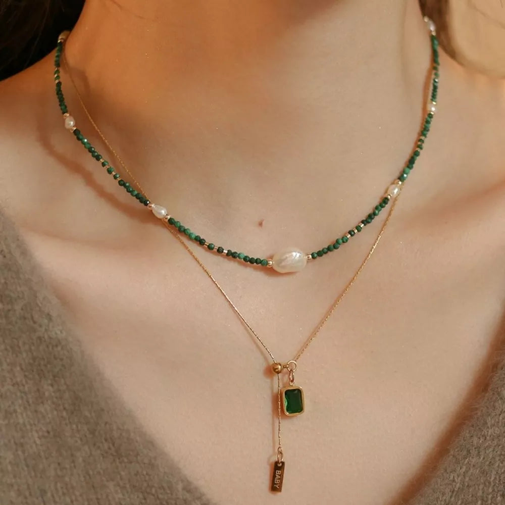 Layered necklace with green malachite beads, freshwater pearls, and a gold chain with emerald pendant.
