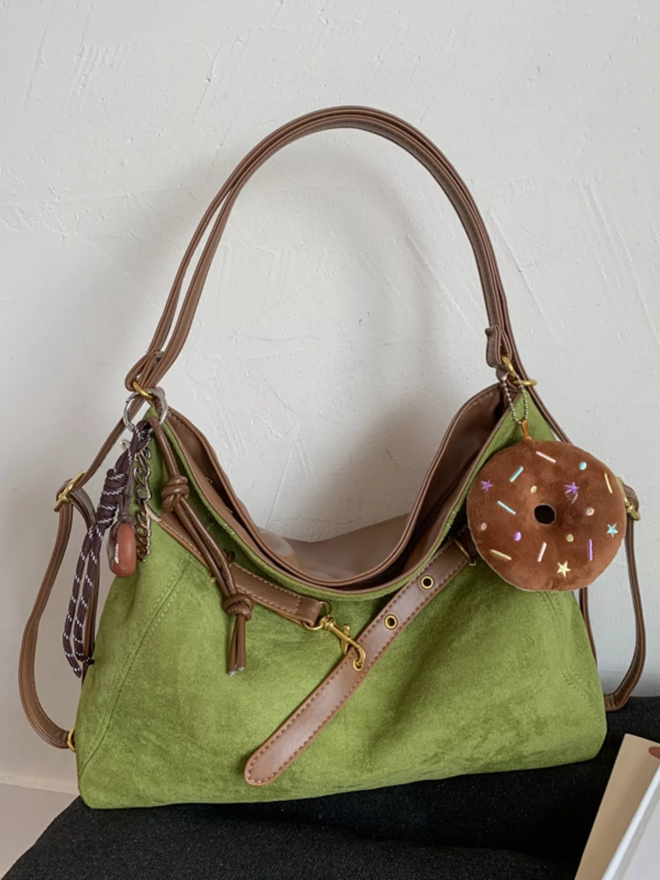 Sage green hobo bag with brown trim, adjustable strap, and donut charm accessory.
