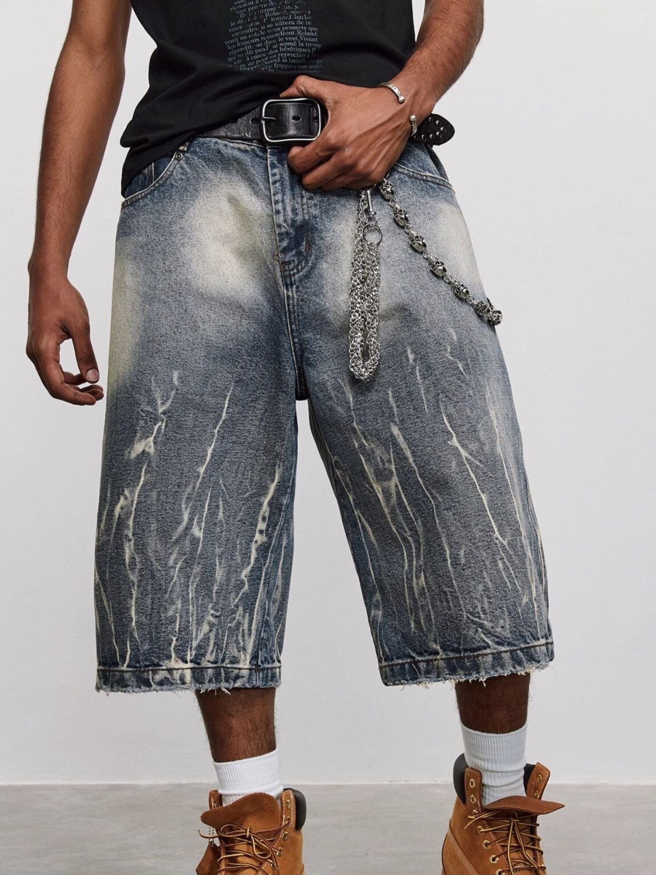 Men's loose fit blue washed denim shorts with distressed details and a chain accessory.