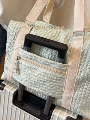 Light green textured travel bag with cream straps and a zippered front pocket.