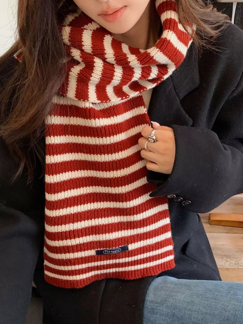 Cozy wool striped winter scarf in deep red and cream, worn by a woman.