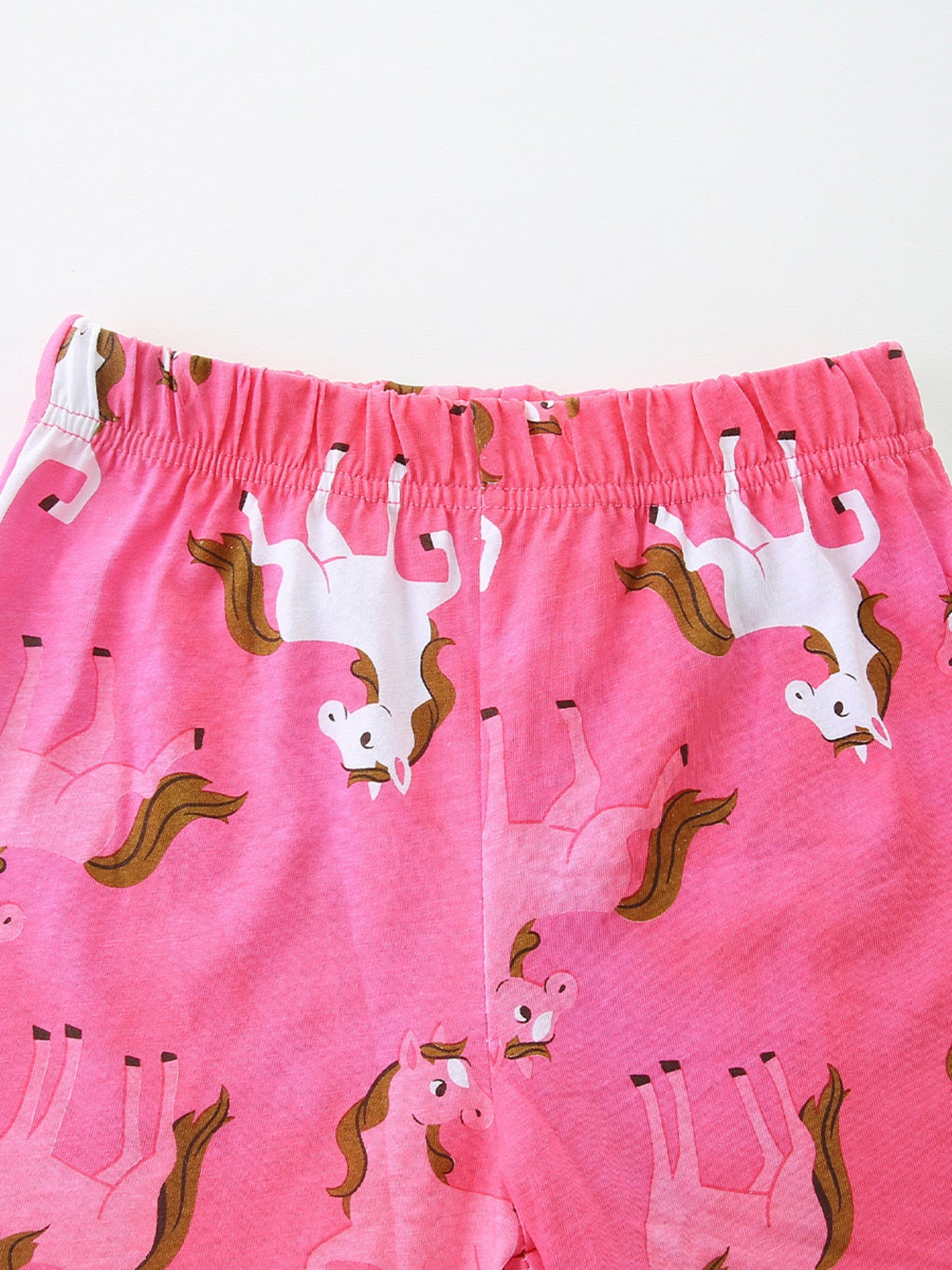 Girls' pink cotton shorts with allover galloping horse print and elastic waistband.