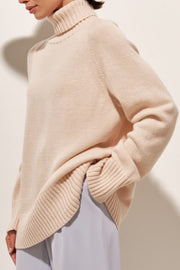 Blush pink cashmere turtleneck sweater with raglan sleeves and ribbed details.