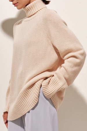 Blush pink cashmere turtleneck sweater with raglan sleeves and ribbed details.