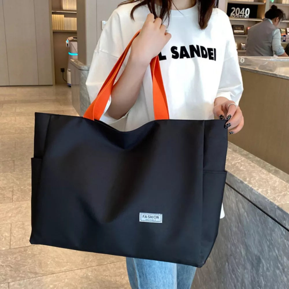 Black canvas shoulder bag with orange straps and side pockets.