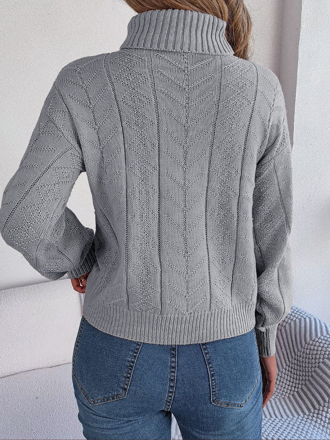 Light gray cable knit turtleneck sweater with drop shoulder and chevron pattern.