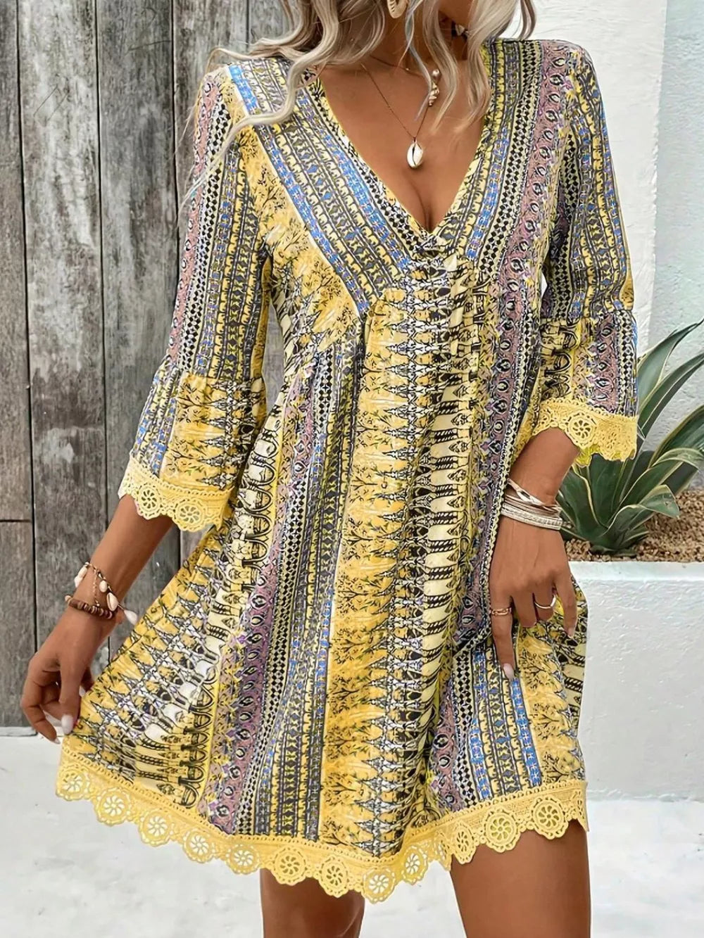 Yellow bohemian v-neck dress with bell sleeves, lace trim, and colorful print.