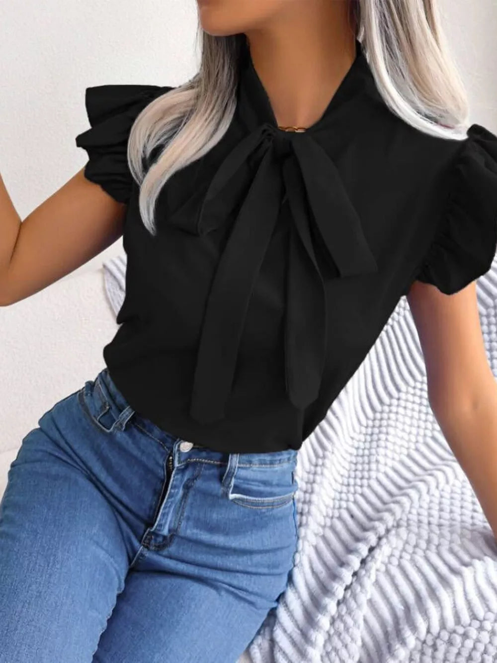 Black pussy-bow blouse with ruffle sleeves and a tie neck, styled with jeans.