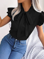 Black pussy-bow blouse with ruffle sleeves and a tie neck, styled with jeans.