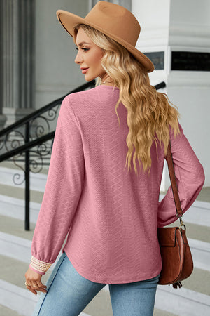 Blush pink textured V-neck blouse with lace trim cuffs and long sleeves.