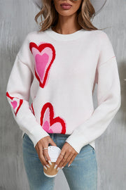White intarsia knit sweater with pink and red heart motif, crew neck, long sleeves.