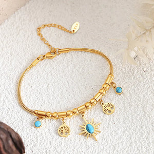 Gold celestial charm bracelet with turquoise accents, featuring sun, tree of life charms and beaded details.