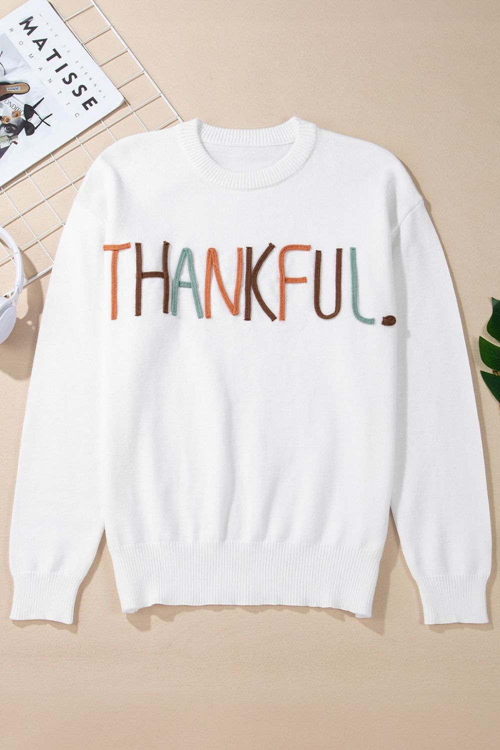 White drop shoulder sweater with embroidered "THANKFUL" text in multi-color yarn.