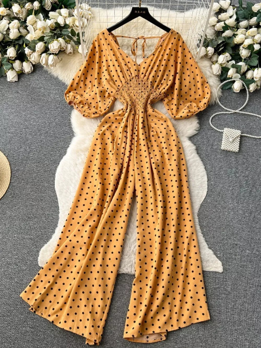 Yellow polka dot smocked wide-leg romper with V-neck and puff sleeves.