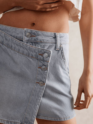 Light blue denim skort with asymmetrical button front and visible stitching.