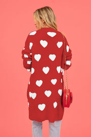 Red acrylic longline cardigan with white heart motif and a red crossbody bag.