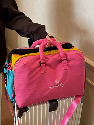 Vibrant pink duffel bag with embroidered sun logo and text, stacked on luggage.