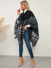 Asymmetric plaid fringe cape in black and grey with a checkered pattern and fringed hem.
