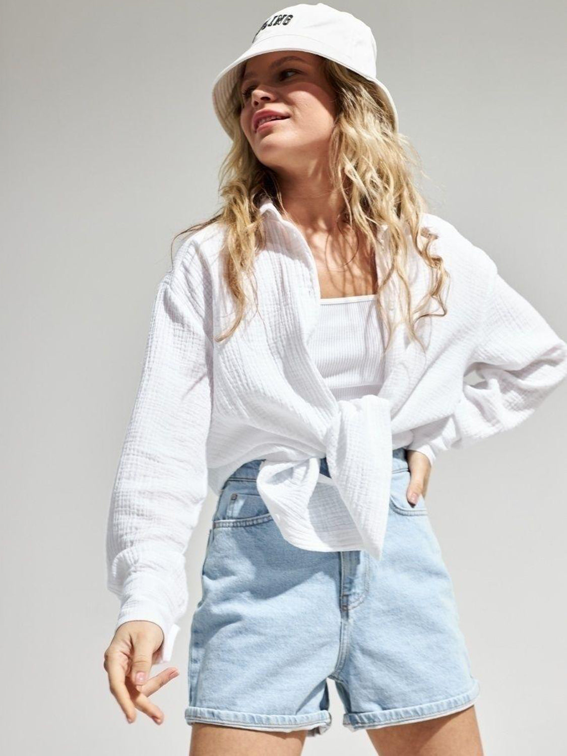 White textured cotton overshirt with relaxed fit, tied at waist, worn over tank top.