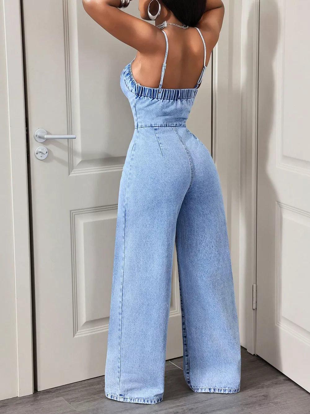 Light wash denim jumpsuit with spaghetti straps, cinched waist, and wide legs.