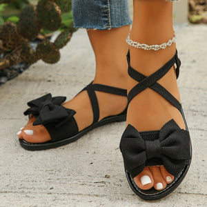 Black crisscross bow sandals with ankle straps and a jeweled anklet.