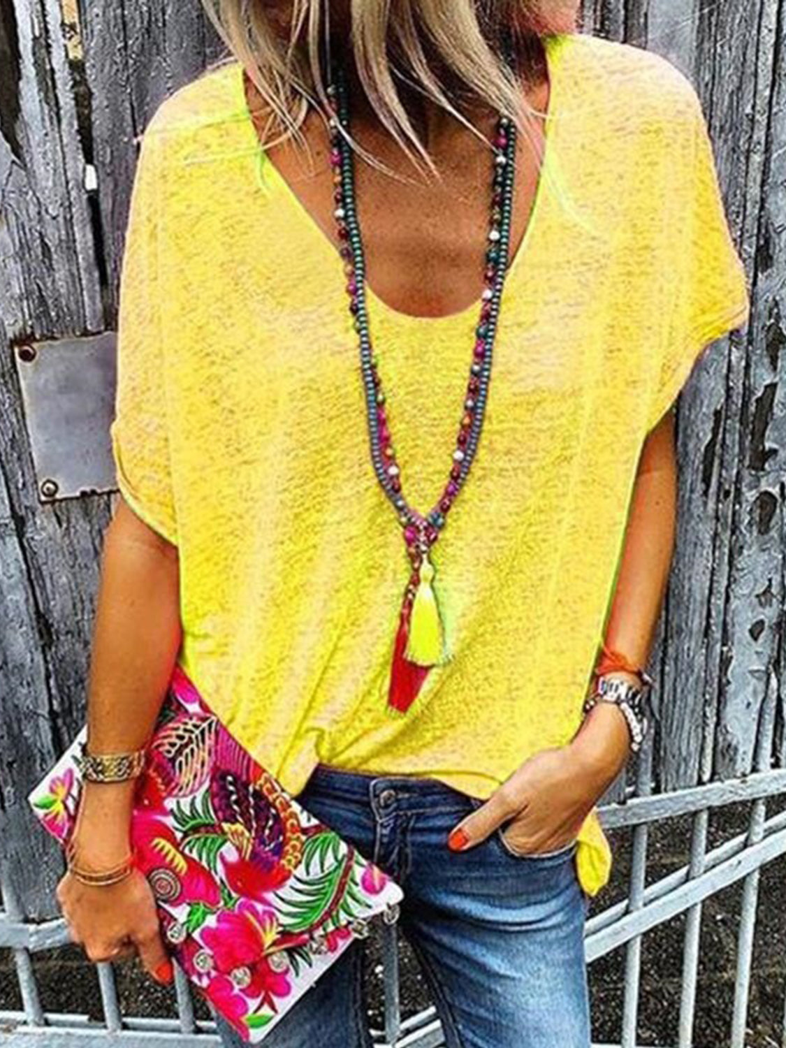 Canary yellow V-neck dolman sleeve tee with rolled cuffs, styled with jeans and a colorful clutch.