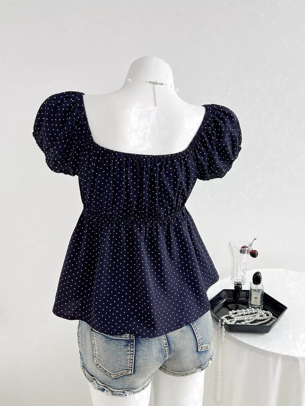 Navy polka dot peplum shirt with puff sleeves and square neckline, styled with denim shorts.