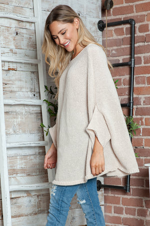 Cream knit sweater with cape sleeves and relaxed fit, styled with jeans.