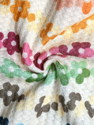Vibrant floral tank top with crochet daisy pattern in pink, orange, green, and brown on white knit fabric.