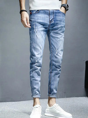 Men's light wash distressed slim fit jeans with ripped details and rolled cuffs.