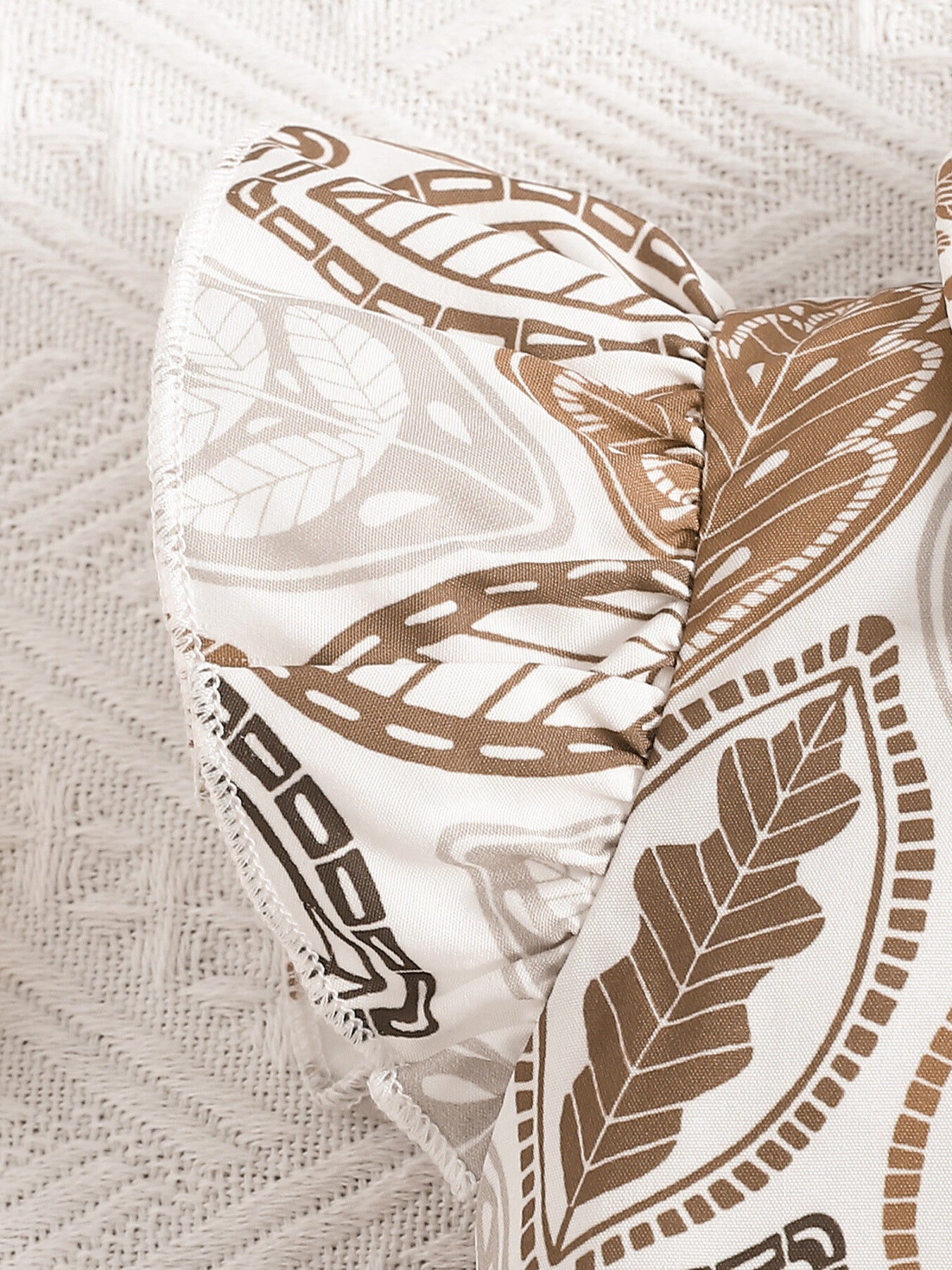 Baby girl's beige leaf print top with ruffled sleeves and bow detail.