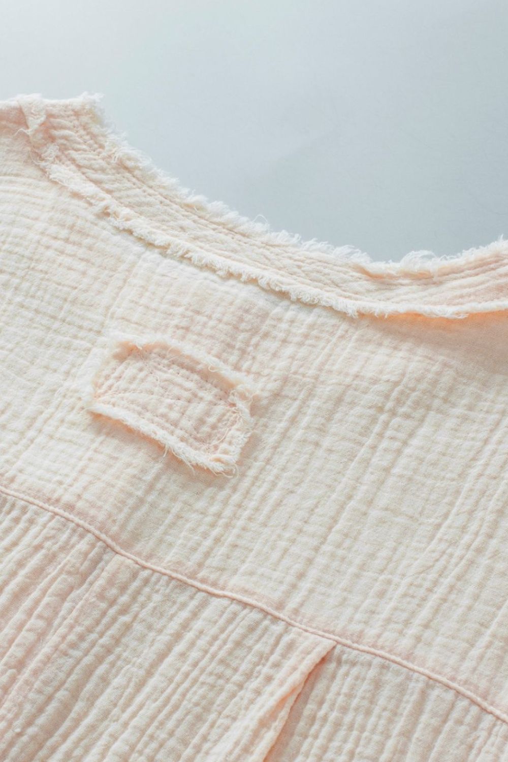 Beige textured gauze henley blouse with raw edge neckline and chest detail.
