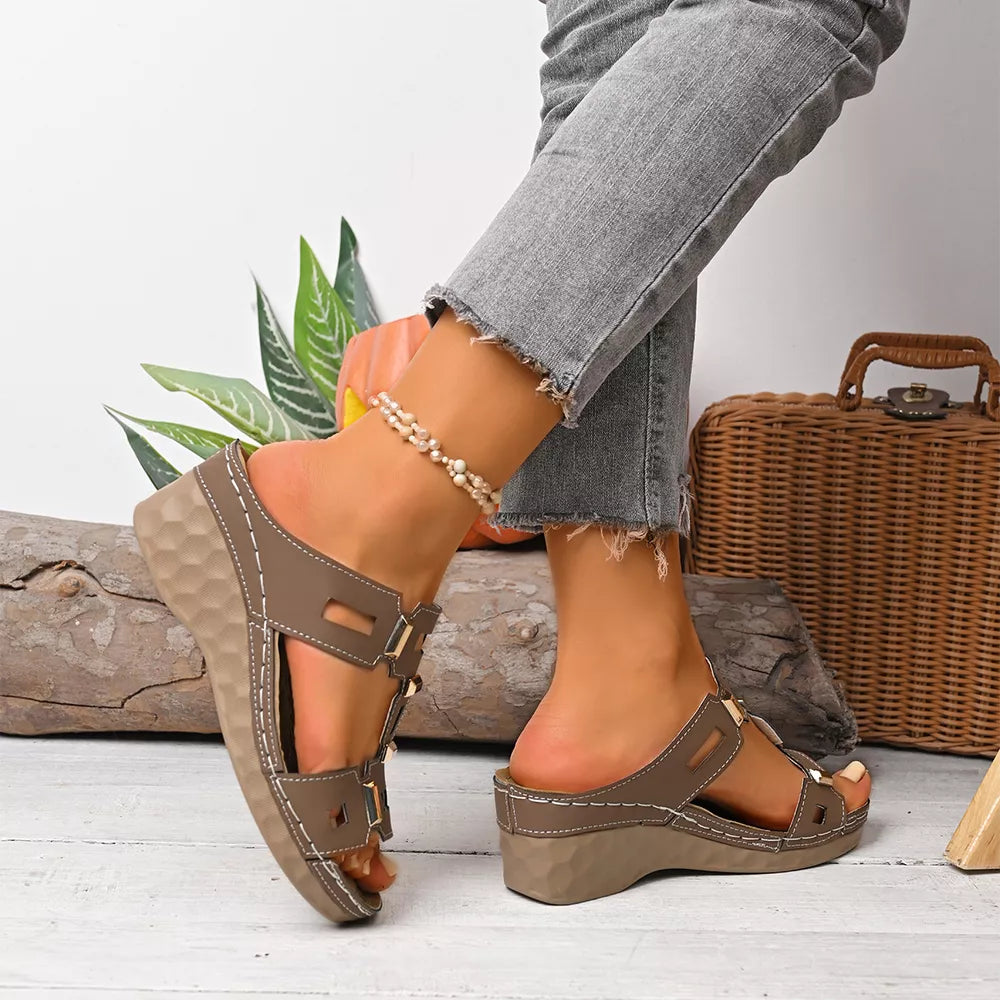Brown open-toe wedge sandals with decorative gold buckles and white stitching.