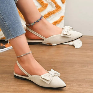 Beige slingback flats with pointed toe and bow detail, styled with anklets.