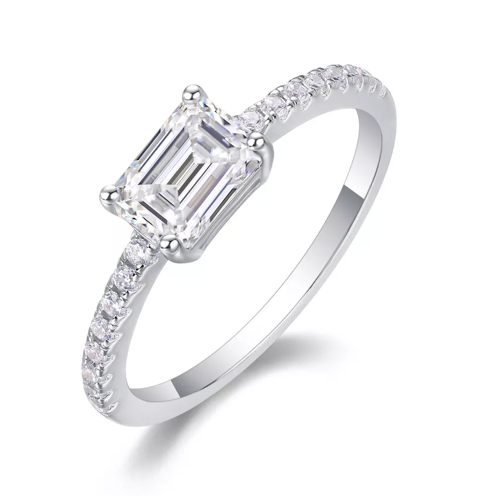 Elegant moissanite ring with emerald-cut center stone and pavé band in sterling silver.