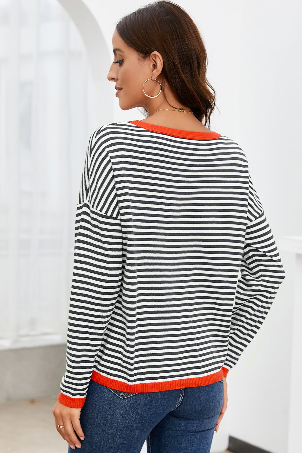 Striped crewneck sweater with contrast orange trim and long sleeves.