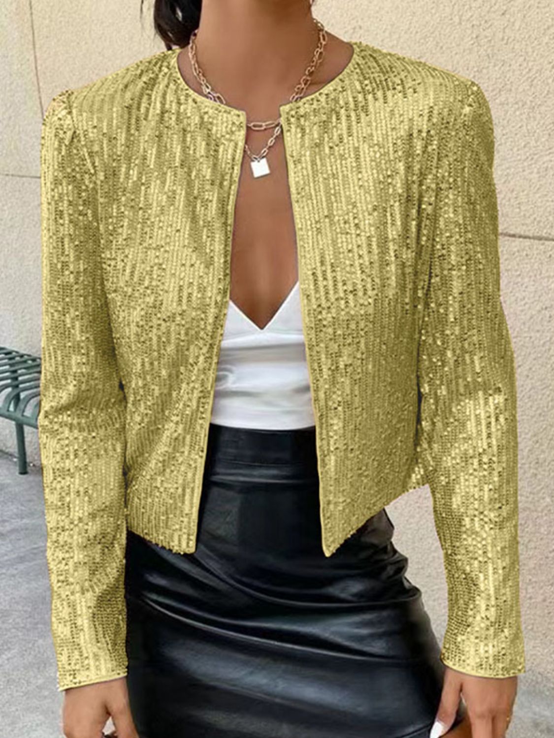 Gold sequin bolero jacket with round neckline and long sleeves, styled with a white top and black skirt.