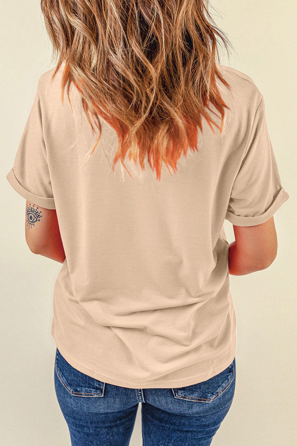 Tan graphic t-shirt with rolled sleeves and a subtle eye tattoo on the arm.