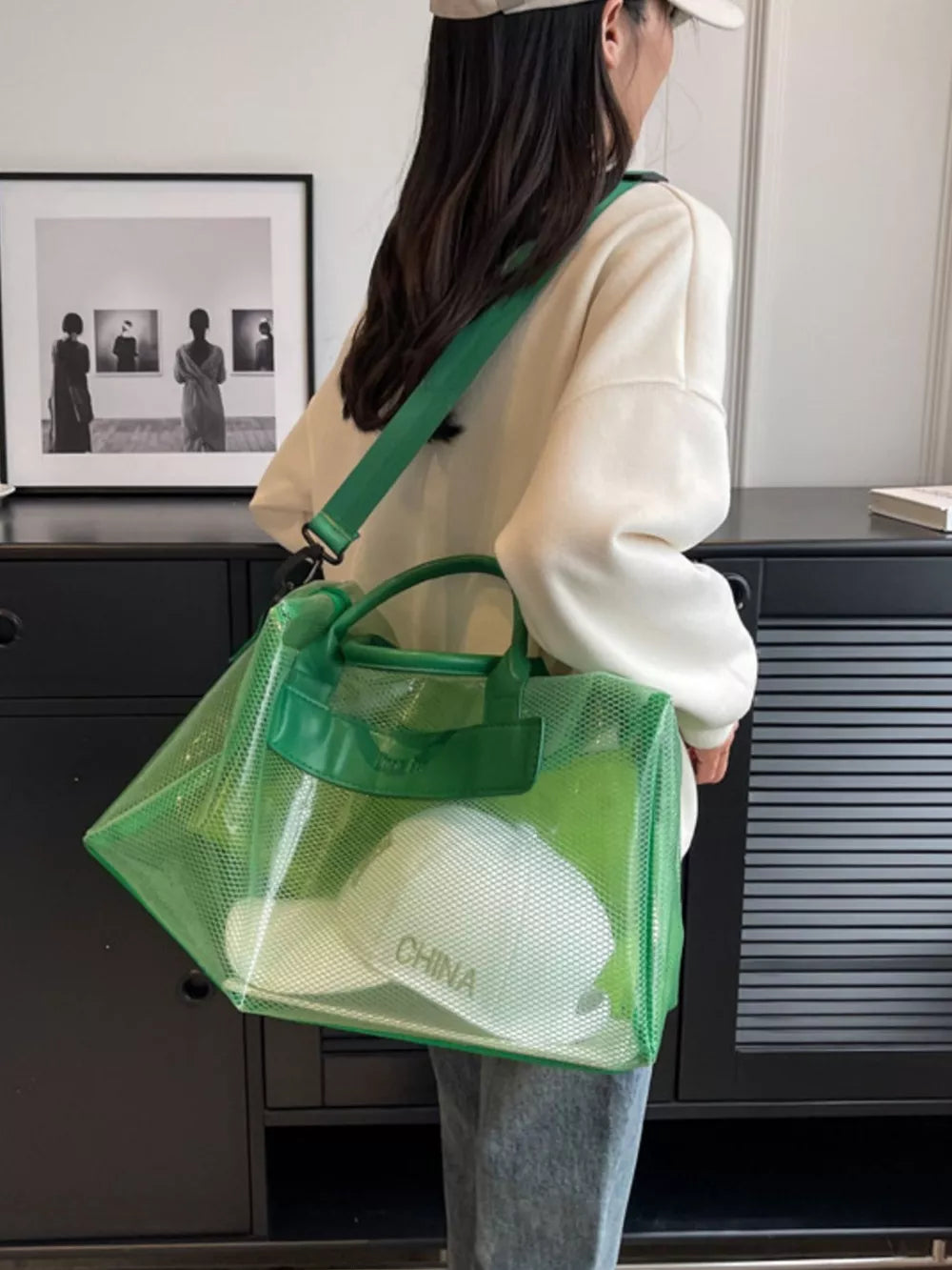 Green transparent PVC mesh travel bag with green straps and handles, showing a white hat inside.