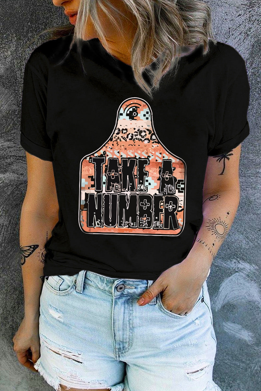 Black graphic t-shirt with "Take A Number" text on a tag shape with abstract pattern.