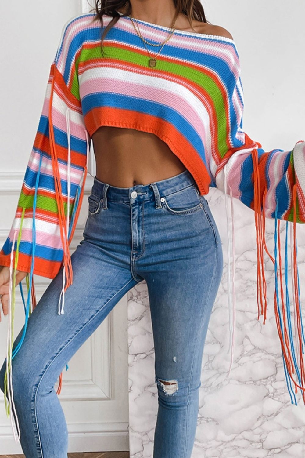 Cropped knit sweater with multicolor stripes and fringe sleeves, off-the-shoulder neckline.