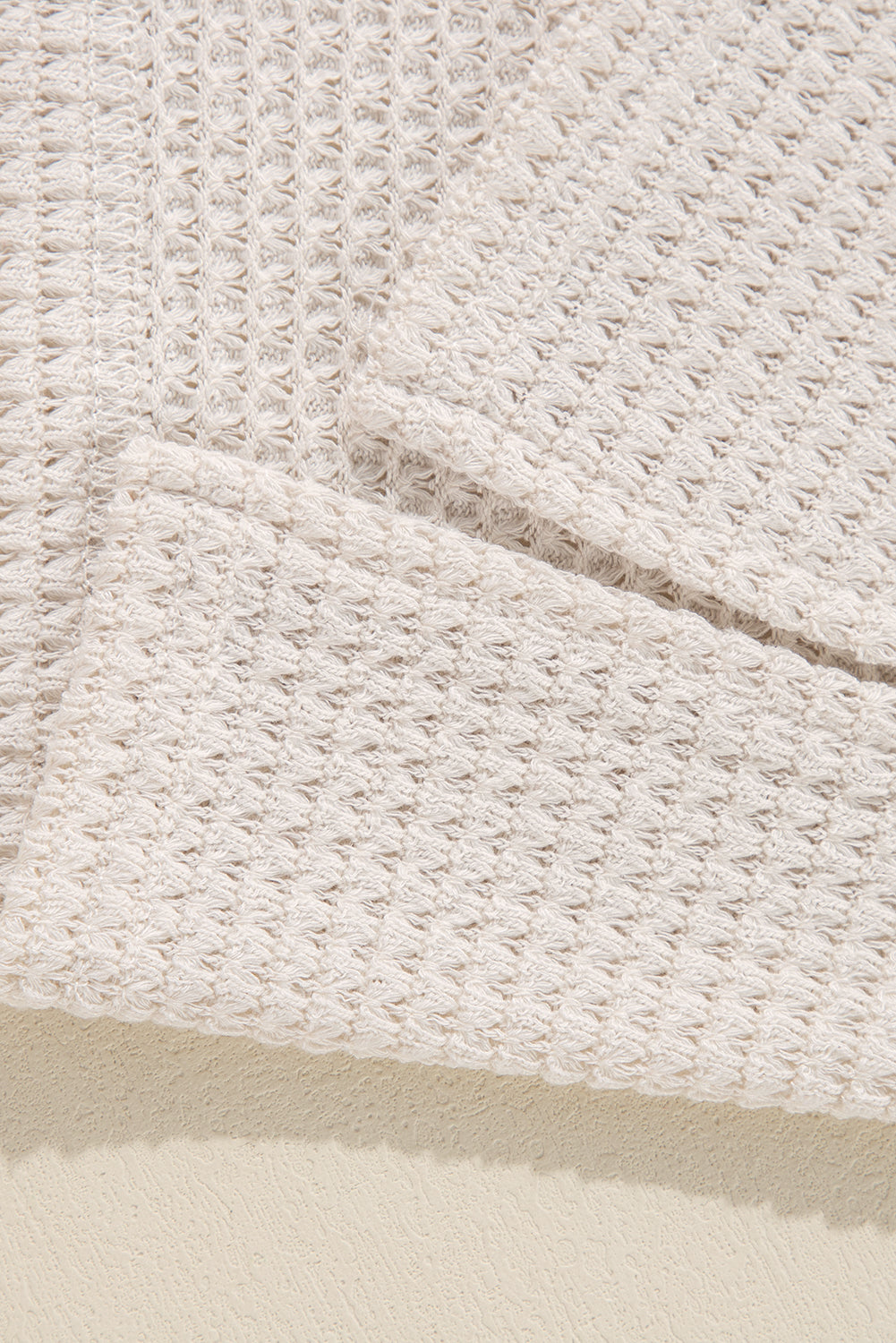 Beige waffle knit V-neck top with slit hem detail.