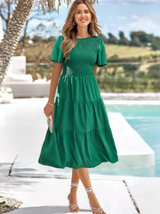 Green smocked tiered midi dress with flutter sleeves and a flowing skirt.
