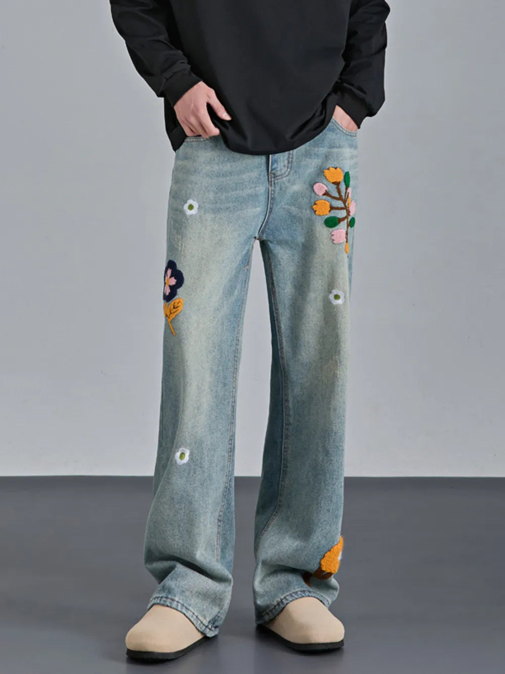 Men's light wash relaxed fit jeans with colorful floral appliques and distressed details.