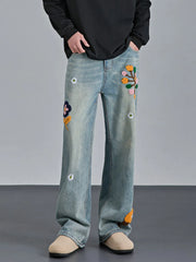 Men's light wash relaxed fit jeans with colorful floral appliques and distressed details.