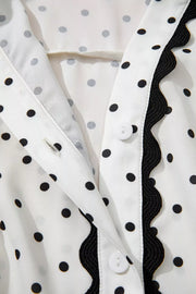 White polka dot midi dress with black scalloped trim and button detail.