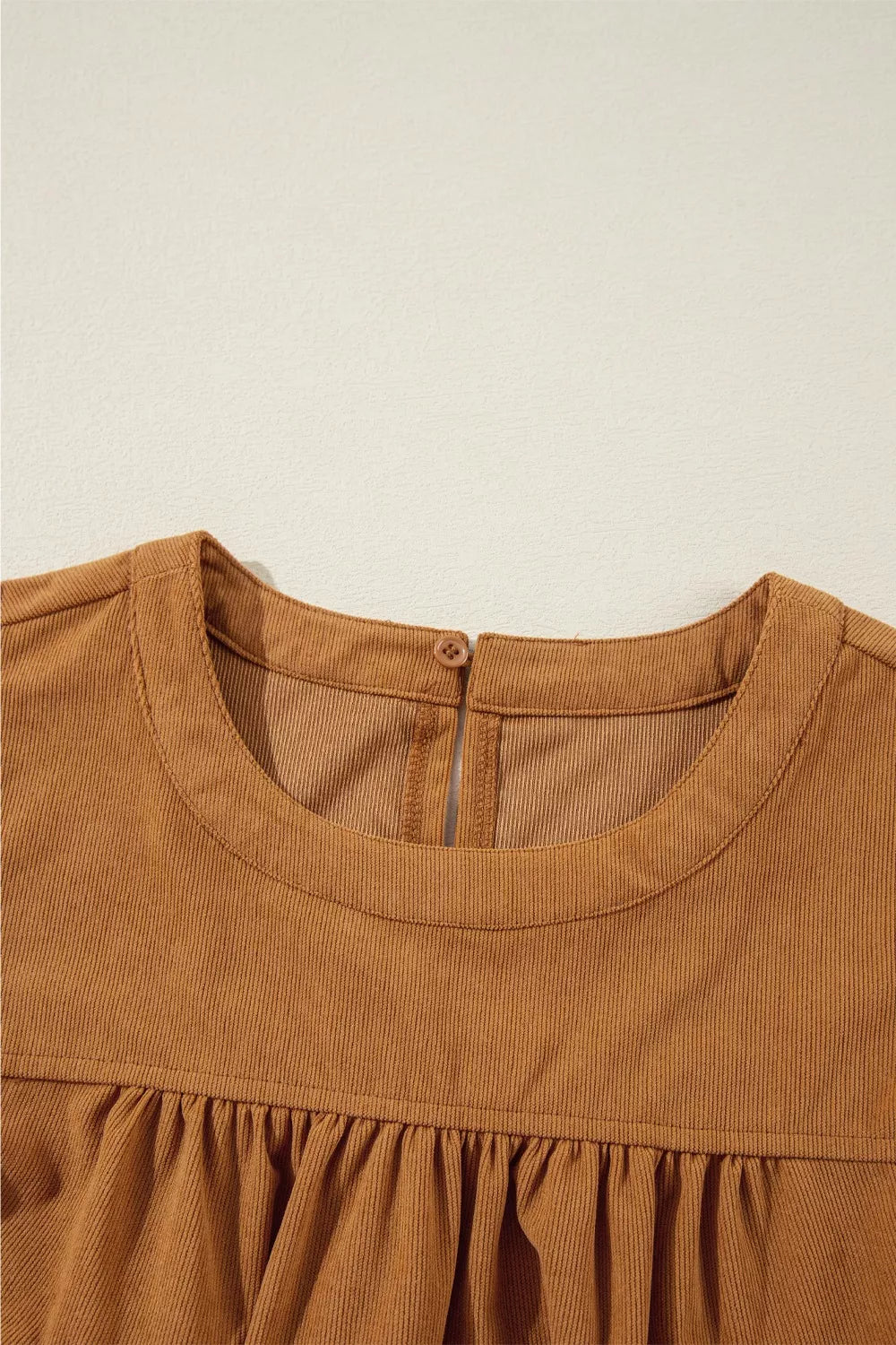 Caramel corduroy babydoll mini dress with round neckline and back button closure.