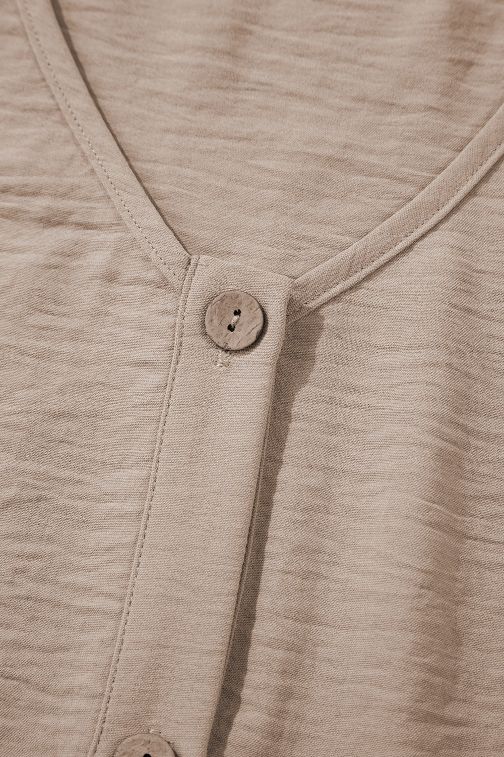 Camel button-front vest detail with textured fabric and wood-look button.