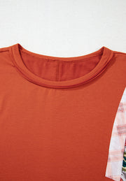 Orange-red blouse with patchwork floral and plaid sleeves and crew neck.